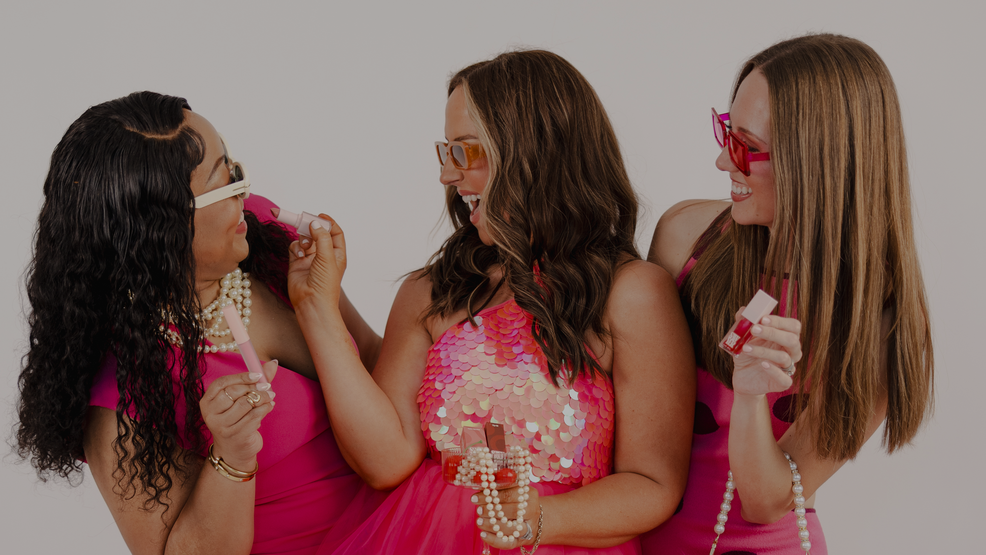 Three women in pink dresses with sunglasses and accessories on a plain background