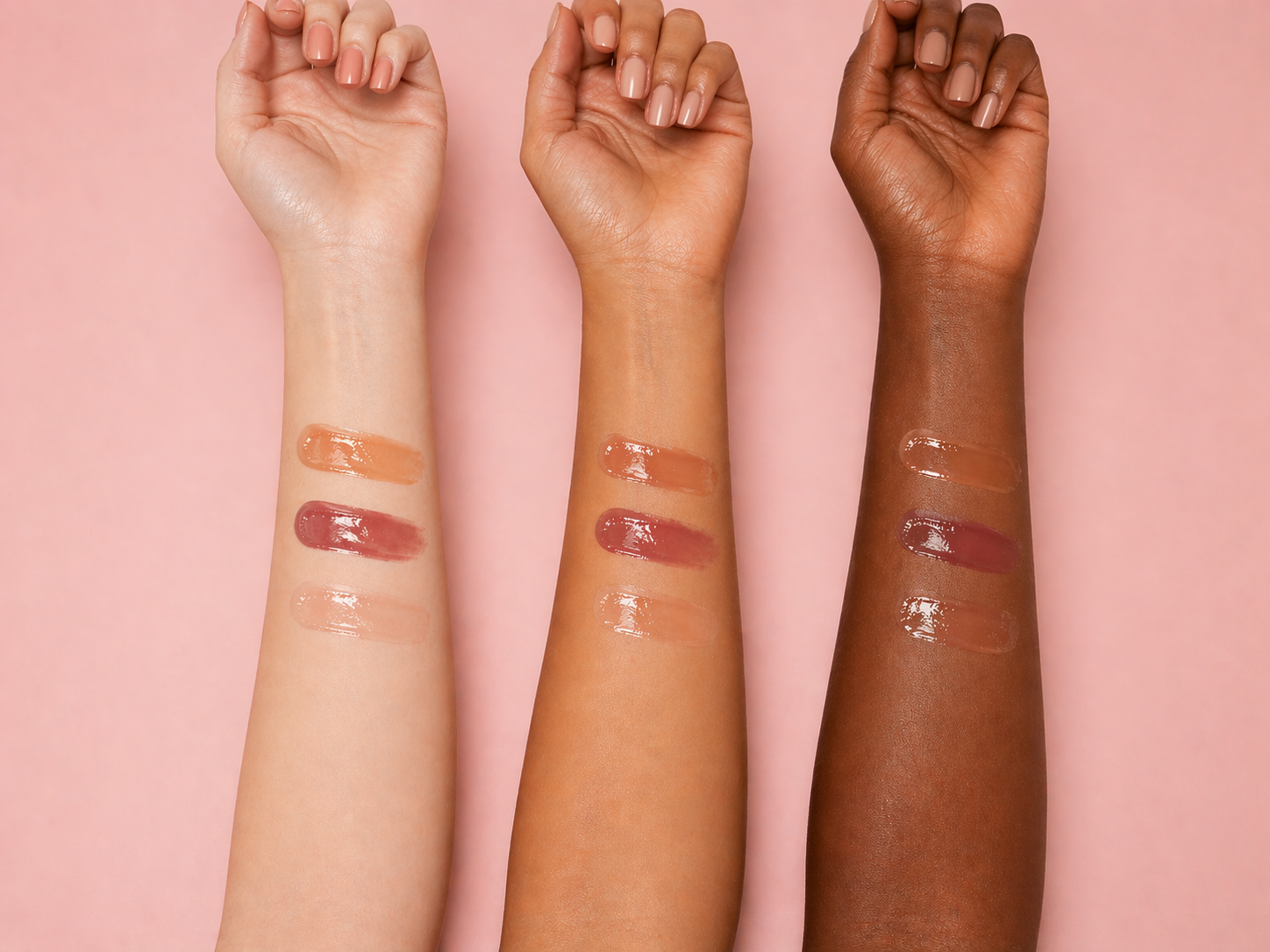 Three arms with different skin tones displaying lip swatches on a pink background